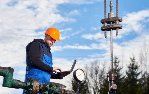 Petroleum engineer using laptop in oil field.